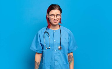 young attractive red hair woman feeling puzzled and confused, with a dumb, stunned expression looking at something unexpected. hospital nurse concept