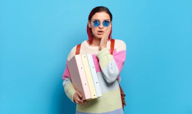 Genç ve çekici kızıl saçlı kadın şok olmuş ve korkmuş hissediyor, ağzı açık ve elleri yanaklarında korkmuş görünüyor. Üniversite öğrencisi konsepti