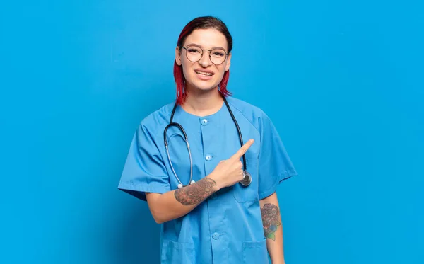 若い魅力的な赤い髪の女性は陽気に笑顔 幸せを感じ 側と上を指して コピースペースにオブジェクトを表示します 病院看護師のコンセプト — ストック写真