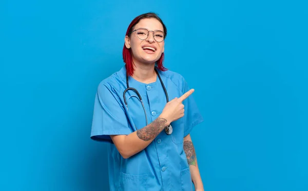 若い魅力的な赤い髪の女性は興奮していると驚いている側と上を指してスペースをコピーします 病院看護師のコンセプト — ストック写真