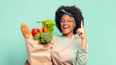 Genç ve güzel afro kadın bir fikri fark ettikten sonra mutlu ve heyecanlı bir dahi gibi hissediyor, neşeli bir şekilde parmağını kaldırıyor, eureka! Ve elinde sebze çantası var.