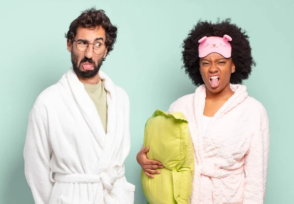 多人種の二人の友人はうんざりしていらいらして舌を突き出し何かを嫌う パジャマと家のコンセプト — ストック写真