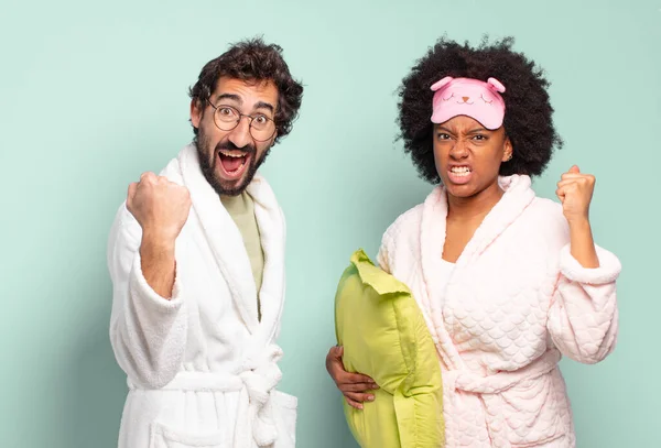 怒りの表情で積極的に叫んでいる友人の多人種のカップルや成功を祝うために握りしめられた拳で パジャマと家のコンセプト — ストック写真