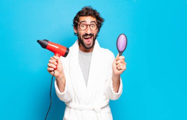 Saç kurutma makinesiyle bornoz giyen genç sakallı adam.