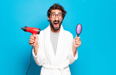 Saç kurutma makinesiyle bornoz giyen genç sakallı adam.