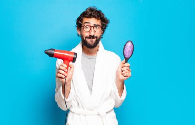 Saç kurutma makinesiyle bornoz giyen genç sakallı adam.