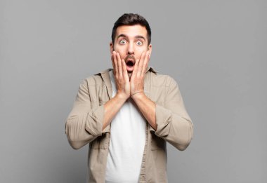 Yakışıklı sarışın adam şok olmuş ve korkmuş hissediyor, ağzı açık ve elleri yanaklarında korkmuş görünüyor.