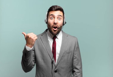 Genç işadamı inançsızlıktan şaşkın şaşkın bakıyor, yan taraftaki objeyi işaret ediyor ve 