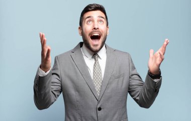 Genç, yakışıklı iş adamı kendini mutlu, şaşkın, şanslı ve şaşırmış hissediyor. Zaferi iki eli havada kutluyor.