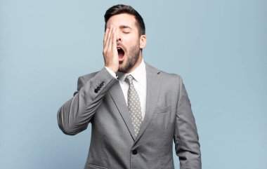 Genç ve yakışıklı iş adamı uykulu görünüyor, sıkılmış ve esniyor, baş ağrısı ve yüzünün yarısını kaplayan bir elle.