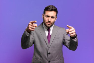 Genç ve yakışıklı iş adamı, kamerayı iki parmağıyla ve kızgın bir ifadeyle sana görevini yapmanı söylüyor.