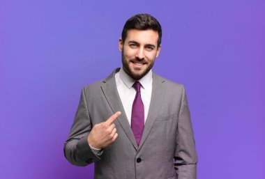Genç ve yakışıklı iş adamı gururlu, kendinden emin ve mutlu görünüyor, gülümsüyor ve kendini işaret ediyor ya da bir numaralı işareti yapıyor.
