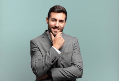 Genç ve yakışıklı iş adamı ciddi, düşünceli ve güvensiz görünüyor, bir kolu çapraz ve çene üzerinde, seçenekleri tartıyor