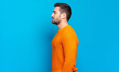 Yakışıklı sarışın adam profil görünümünde. İlerideki boşluğu kopyalamak istiyor. Düşünüyor, hayal ediyor ya da hayal ediyor.