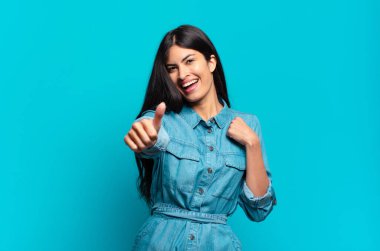 Genç Latin asıllı sıradan bir kadın gururlu, tasasız, kendinden emin ve mutlu, başparmağıyla olumlu gülümsüyor.