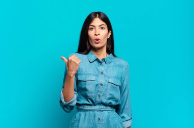 Genç Latin asıllı sıradan bir kadın inançsızlıktan şaşkın şaşkın bakıyor, yan taraftaki objeyi işaret ediyor ve 