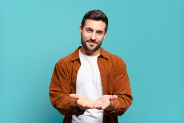 Yakışıklı yetişkin sarışın adam mutlu bir şekilde gülümsüyor, arkadaş canlısı, kendinden emin, pozitif bakışlı, bir nesne ya da konsept sunuyor ve gösteriyor.