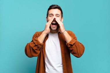 Yakışıklı sarışın adam mutlu, heyecanlı ve pozitif hissediyor. Elleri ağızda, bağırıyor.