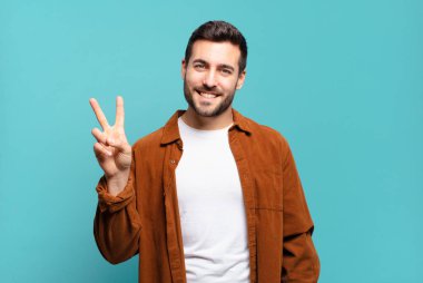 Yakışıklı sarışın adam gülümsüyor ve arkadaş canlısı görünüyor. İki ya da iki numarayı gösteriyor. Elleri önde, geriye doğru sayıyor.