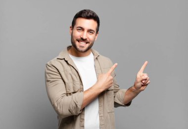 Yakışıklı yetişkin sarışın adam mutlu bir şekilde gülümsüyor ve her iki elini de fotokopi alanında objeler gösteriyor.