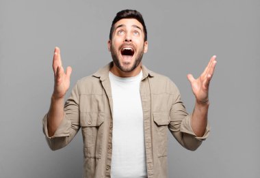 Yakışıklı sarışın adam mutlu, şaşkın, şanslı ve şaşırmış hissediyor. Zaferi iki eli havada kutluyor.