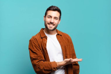 Yakışıklı, sarışın, neşeli bir şekilde gülümseyen, mutlu hisseden ve fotokopi uzayında avuç içiyle bir konsept gösteren bir adam.