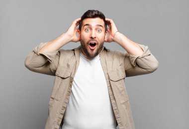 Yakışıklı sarışın adam heyecanlı ve şaşırmış görünüyor, ağzı açık, iki eli başında, kendini şanslı hissediyor.