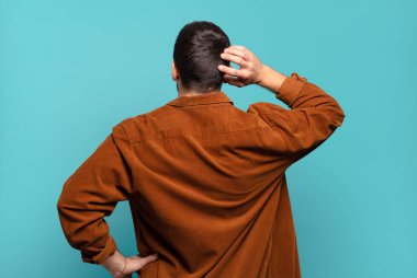 Yakışıklı sarışın adam düşünüyor ya da şüphe ediyor, kaşınıyor, kafası karışık ve kafası karışık, arkaya ya da arkaya bakıyor.