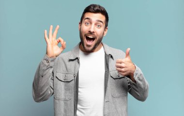 Yakışıklı yetişkin sarışın adam mutlu, şaşkın, tatmin olmuş ve şaşırmış hissediyor, iyi ve güzel hareketler gösteriyor, gülümsüyor.