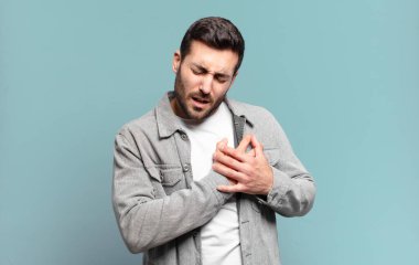 Yakışıklı sarışın adam üzgün, yaralı ve kalbi kırık görünüyor, iki elini de kalbe yakın tutuyor, ağlıyor ve bunalımda.