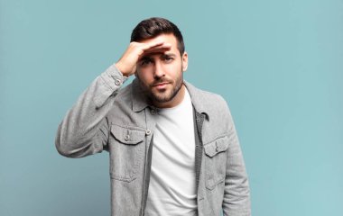 Yakışıklı yetişkin sarışın adam şaşkın ve şaşkın bakıyor, el üstünde uzak bakıyor, izliyor ya da arıyor