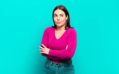 Genç ve güzel bir kadın omuz silkiyor, kafası karışık ve kararsız, kolları bağlı ve şaşkın görünüyor.