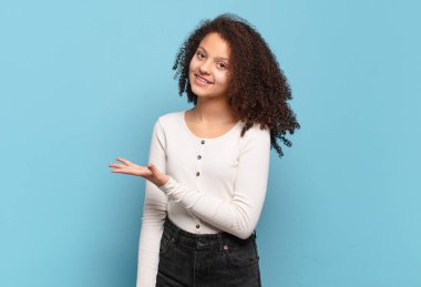  Neşeli bir şekilde gülümsüyor, mutlu hissediyor ve bir konsepti fotokopi uzayında avuç içiyle gösteriyor.