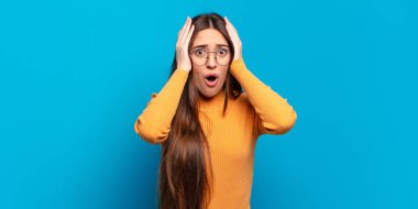 Genç, hoş, hoş olmayan, şaşkın, korkmuş ya da endişeli görünen, ağzı açık ve iki kulağını da elleriyle kapatan bir kadın.