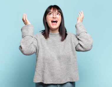 Artı boyut olarak güzel bir kadın mutlu, şaşkın, şanslı ve şaşırmış hissediyor, zaferi iki eli havada kutluyor.