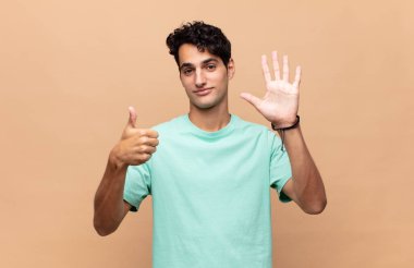 Genç yakışıklı adam gülümsüyor ve arkadaş canlısı görünüyor, altı ya da altıncı numarayı gösteriyor, eli önde, geri sayıyor.