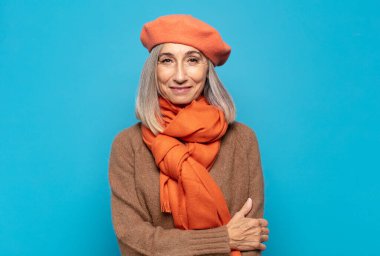 Orta yaşlı bir kadın utangaç ve neşeli bir şekilde gülüyor, arkadaş canlısı ve olumlu ama güvensiz bir tavırla. 