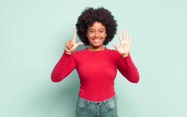  Gülümsüyor ve dost canlısı görünüyor, 7 ya da 7 numarayı gösteriyor, elleri önde, geri sayıyor.