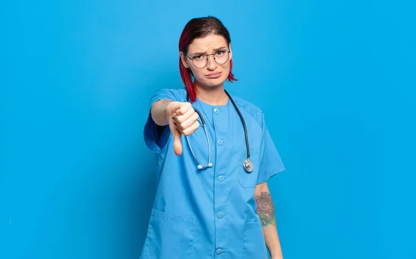 若い魅力的な赤い髪の女性は 深刻な表情で親指を下に示す クロス いらいら 失望や不満を感じている 病院看護師のコンセプト — ストック写真