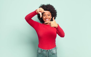  Mutlu, arkadaş canlısı ve pozitif hissediyorum, gülümsüyor ve elleriyle bir portre veya fotoğraf çerçevesi yapıyor.