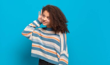  Gülümsüyor, tuhaf bir şekilde yan tarafa bakıyor, dedikoduları dinlemeye ya da bir sırrı duymaya çalışıyor.