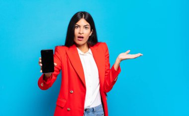 Genç İspanyol kadın şaşkın ve şaşkın hissediyor, şüpheci, farklı seçenekleri tartıyor ya da komik bir ifadeyle seçiyor. telefon ekran kopyalama alanı