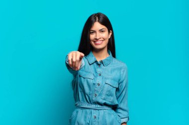 Genç Latin asıllı sıradan bir kadın kameraya tatmin olmuş, kendinden emin, dostane bir gülümsemeyle bakıyor ve seni seçiyor.