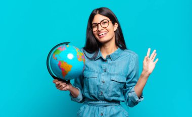 Genç İspanyol kadın mutlu ve neşeli bir şekilde gülümsüyor, el sallıyor, sizi selamlıyor ve selamlıyor, ya da veda ediyor. Toprak gezegeni konsepti