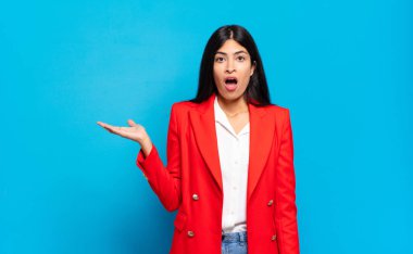 Genç İspanyol iş kadını şaşırmış ve şoka uğramış görünüyor, çenesi düşmüş, elinde açık bir elle bir nesne tutuyor.