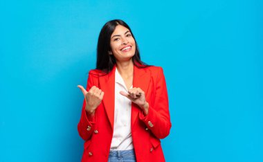 Genç İspanyol iş kadını neşeli bir şekilde gülümsüyor ve yan taraftaki fotokopi alanını gösteriyor, mutlu ve tatmin olmuş hissediyor.