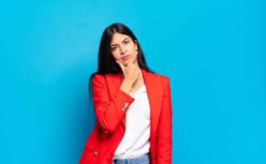 Genç İspanyol iş kadını ciddi, düşünceli ve güvensiz görünüyor, bir kolu çapraz ve çene üzerinde, seçenekleri tartıyor