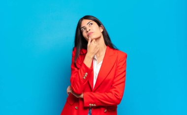 Genç İspanyol iş kadını düşünceli, meraklı ya da hayalperest hissediyor, hayal kuruyor ve mekanı kopyalamak için yukarı bakıyor.