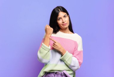 Genç ve güzel İspanyol bir kadın sabırsız ve kızgın görünüyor, saati gösteriyor, dakiklik istiyor, zamanında gelmek istiyor.