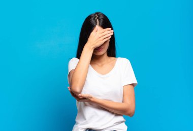 Genç, güzel, İspanyol bir kadın stresli, utanmış ya da üzgün görünüyor. Başı ağrıyor, yüzünü eliyle kapatıyor.